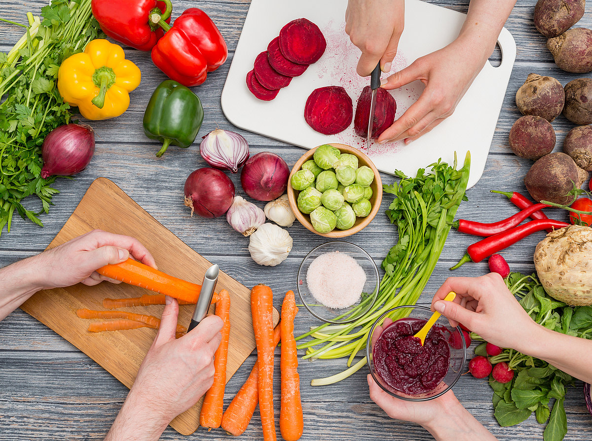 Hände, die verschiedenes Gemüse zum Kochen schälen und vorbereiten