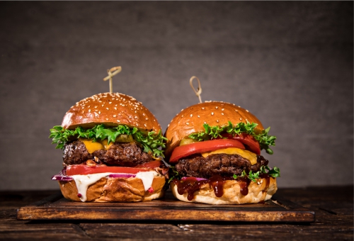 Zwei Cheeseburger mit Salat und Tomaten auf einem Holzbrett