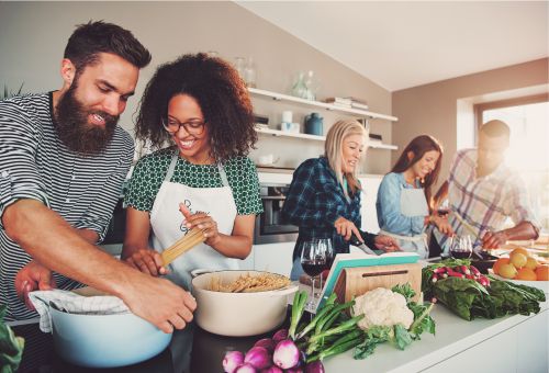 Drei Frauen und zwei Männer kochen in einer Küche Nudeln und Sauce.