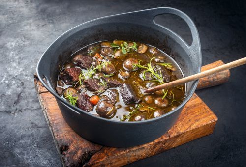 Eintopf mit Rindfleisch, Karotten und Zwiebeln in Rotwein-Soße in gusseisernem Topf