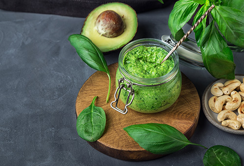 Grünes Pesto aus Basilikum und Avocado in Glasbehälter auf einem Tisch