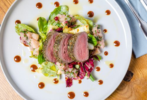 Rehrücken aus dem Smoker, Feldsalat und Radicchio mit Balsamico-Preiselbeer-Vinaigrette und Birnen-Chutney auf einem weißen Teller angerichtet