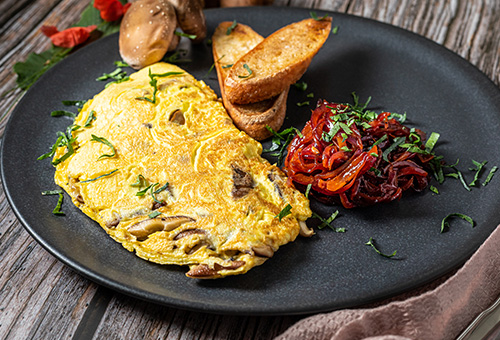 Omlette mit Shiitake-Pilzen auf einem Teller mit Zwiebelmarmelade und Knoblauchbrot angerichtet