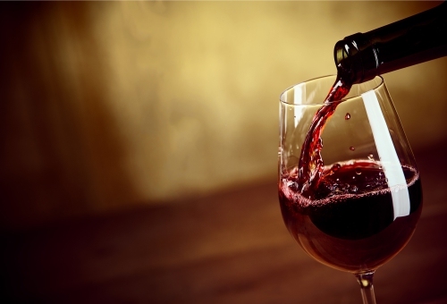 Rotwein wird in ein Weinglas eingeschenkt, das auf einem Holztisch steht