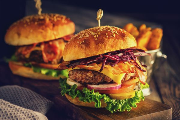 Zwei Cheesburger auf einem Holzbrett und Pommes in einer Schale dahinter