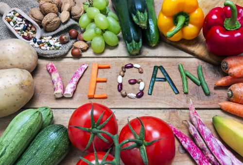 Buchstaben aus Gemüse ergeben auf einem Tisch das Wort Vegan, drum herum verschiedenes Gemüse als Deko