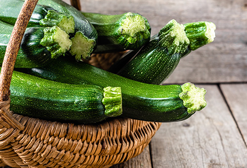 Wissenswert-zucchini-korb Mehrere grüne Zucchini in einem geflochtenem Korb auf einem Holzuntergrund.
