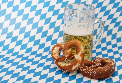 Ein gefüllter Bierkrug aus Glas und zwei Brezeln auf einer blau weiß karierten Tischdecke