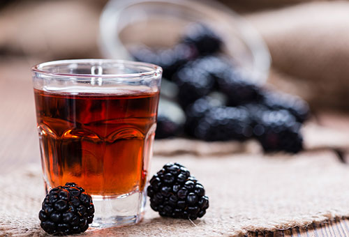 Brombeerlikör in einem Schnapsglas Frischer Brombeerlikör in einem Schnapsglas mit danebenliegenden Brombeeren