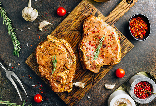 Frisches Steak mariniert mit einer Marinade auf einem Holzbrett garniert mit frischem Rosmarin