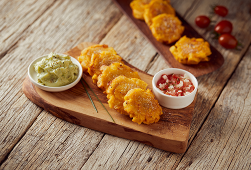 Frittierte Kochbanenenscheiben auf einem Holzbrett mit Salsa und Guacamole