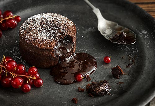 Schokoladenlavakuchen mit flüssigem Kern und Johanissbeeren angerichtet Schokoladenlavakuchen mit flüssigem Kern und Johanissbeeren angerichtet