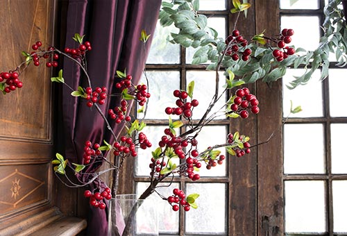 weihnachtlicher Holzzweig mit roten Beeren vor einem alten Fenster mit Gardine