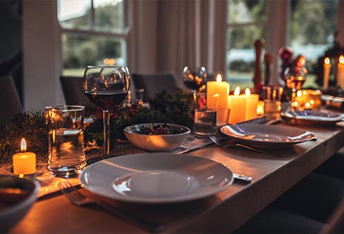 nachhaltig gedeckte Weihnachtstafel mit Kerzen, Tannengrün und weißem Geschirr sowie Gläsern