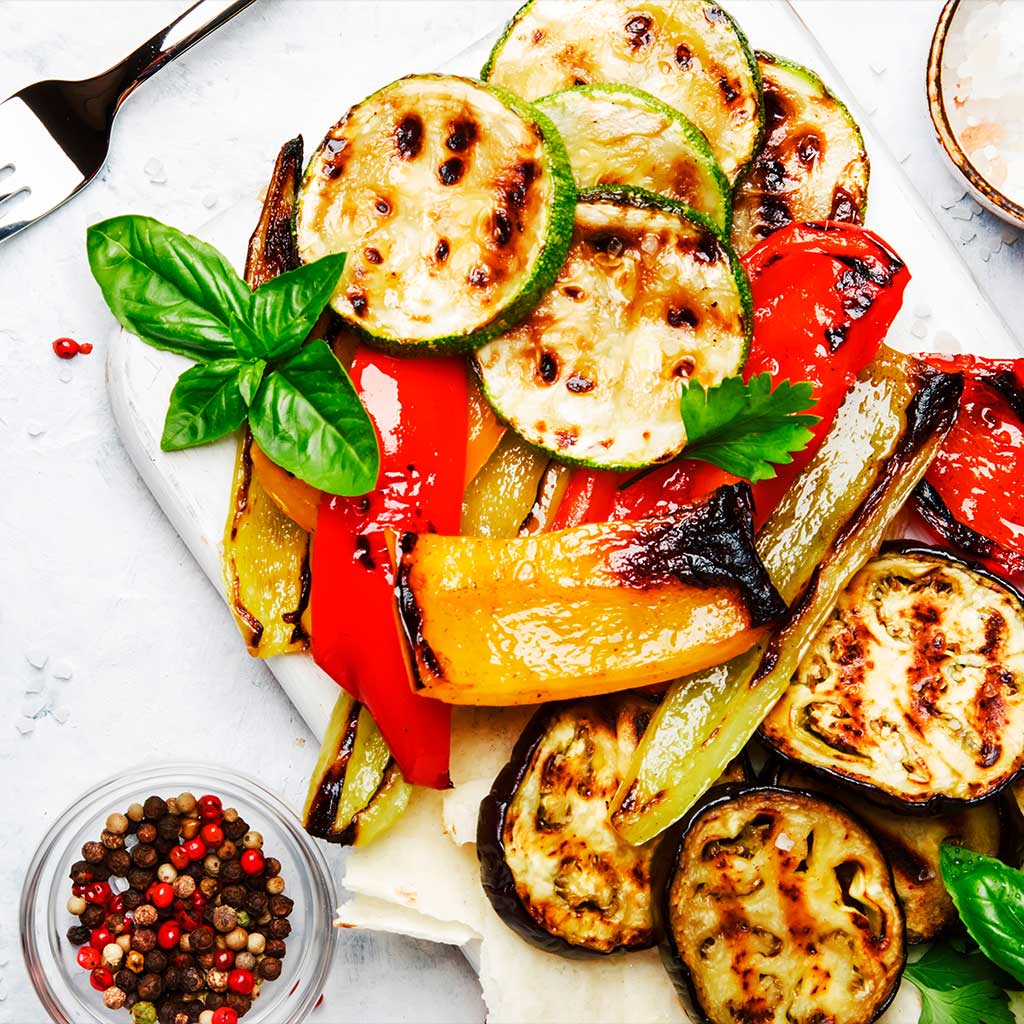 Grillgemüse serviert auf einer weißen Platte mit gewürzen und Pfeffer. Zucchini, Aubergine, Paprika vom Grill garniert mit Basilikum.