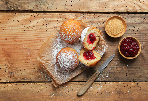 Mi Marmelade gefüllte Berliner auf Holzuntergrund, daneben eine Schüssel Marmelade und Zucker