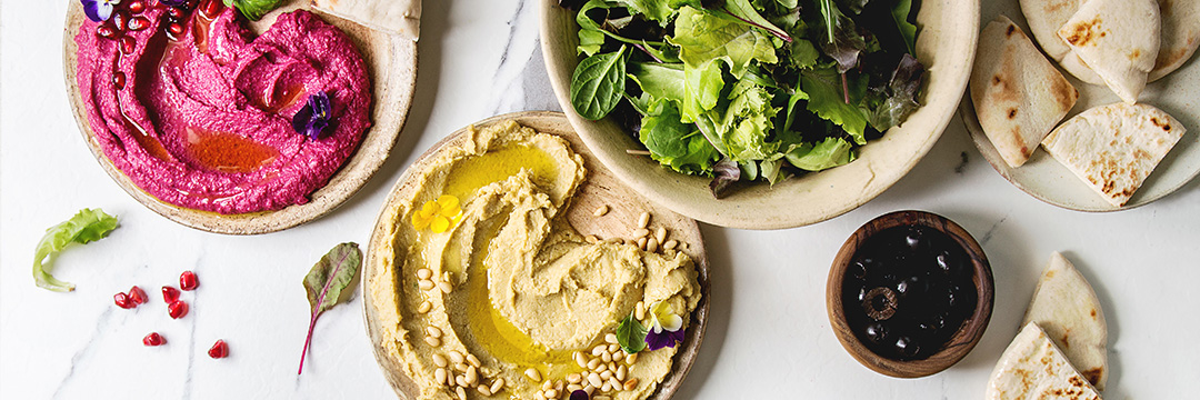 Hummus, Roter Brotaufstrich, Salat, Oliven und Pita-Brot auf einem Tisch