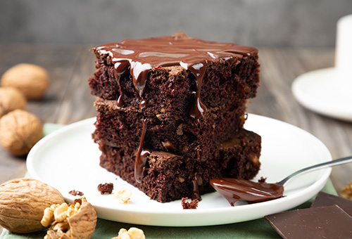 Klassische Brownies mit Schokolade Drei Brownie-Stücke übereinander gestapelt und mit Schokolade übergossen auf einem Teller