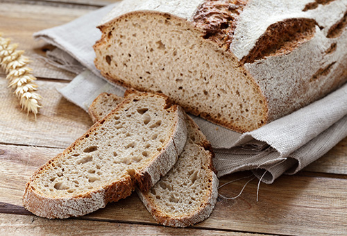 Zwei Scheiben Sauerteigbrot vor einem Laib Sauerteigbrot