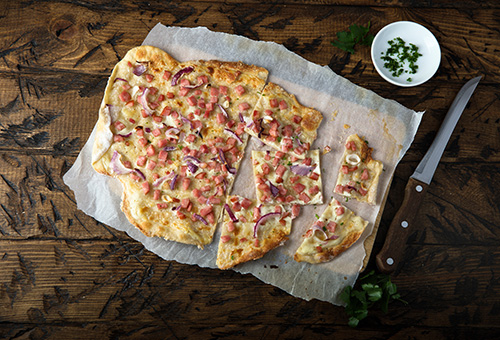 Original Elsässer Flammkuchen mit Zwiebel & Speck Elsässer Flammkuchen mit Zwiebel & Speck auf einem Holzbrett