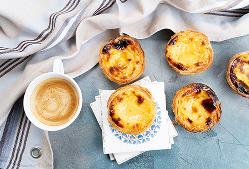 Pastéis de Nata auf einem Tisch mit einer Tasse Kaffee