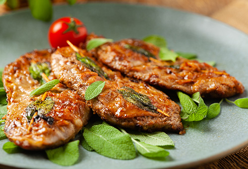 Saltimbocca alla Romana auf einem Teller mit Salbei angerichtet Saltimbocca alla Romana auf einem Teller mit Salbei angerichtet