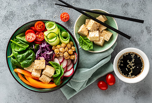 Tiefer Teller mit gebratenem Tofu, Tomaten, Salatgurke, Kichererbsen, Paprika und grünem Salat