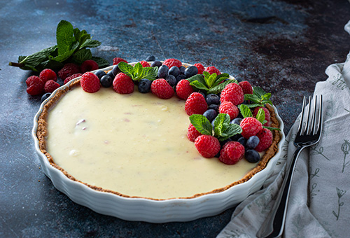 Weiße Schokoladen Vanille Tarte mit Himbeermarmelade in Tarteform und Beeren als Dekoration auf Tisch