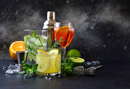Auswahl verschiedener Aperitifs Drei verschiedene Aperitifs auf einem dunklen Tisch, im Hintergrund Zubehör zum Mixen von Getränken
