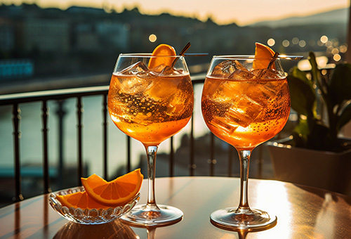 Aperol Spritz Zwei Gläser Aperol Spritz auf einem Tisch auf einem Balkon mit Blick über einen Fluss im Sonnenuntergang