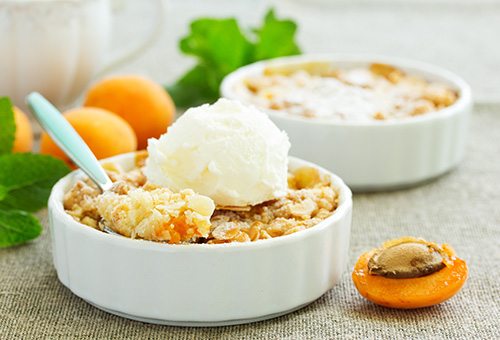 Aprikosencrumble Aprikosencrumble in zwei kleinen Auflaufförmchen mit einer Kugel Vanilleeeis