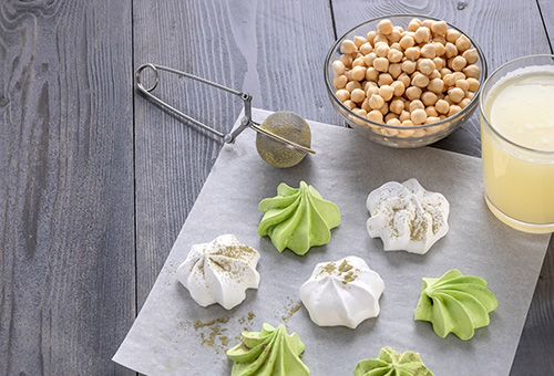 Vegane Matcha-Baisers Vegane Matcha-Baisers aus Aquafaba, Aquafaba und Kichererbsen in Schüsseln im Hintergrund