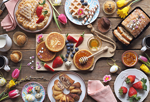 Tisch mit Pancakes, Sirup, Waffeln mit Puderzucker, verschiedene Kuchen, Erdbeeren und Muffins
