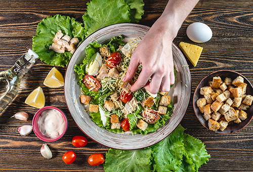 Koch bereit einen Ceasar Salad zu und drapiert die Croutons auf dem Salad