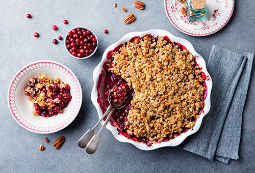 Cranberrycrumble in einer Auflaufform Cranberrycrumble in einer weißen Auflaufform, daneben eine Schüssel mit Cranberries