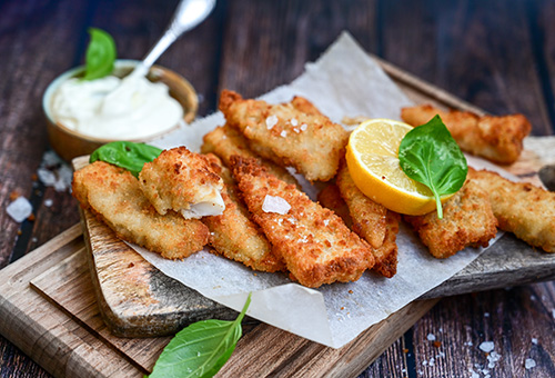 Backfisch, in Teig frittierter Fisch, auf einem Holzbrett mit Mayonaise im Hintergrund