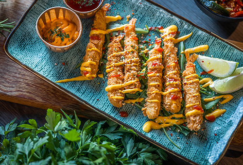 Tempura-Garnelen auf einem blauen Teller mit Dip und Zitrone garniert