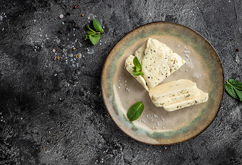 Frischer Halloumi Frischer Halloumi am Stück und eine Scheibe, die beide auf einem grauen Teller liegen
