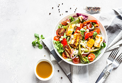 Salat mit gegrilltem Halloumi Salat mit gegrilltem Halloumi in einer weißen Schüssel, daneben ein Schälchen mit Dressing