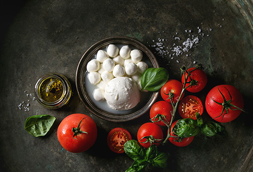 Büffelmozzarella in einer Schüssel und Tomaten vor dunklem Hintergrund