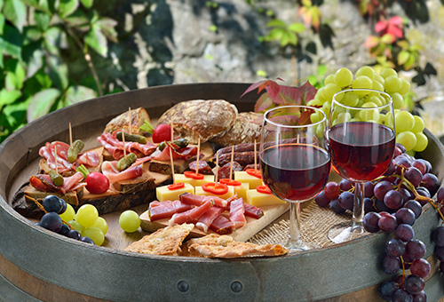 Beim Törggelen in Südtirol mit den Schinken, Kaminwurzen, Käse und Schüttelbrot auf einem Weinfass angerichtet und dazu regionaler Rotwein