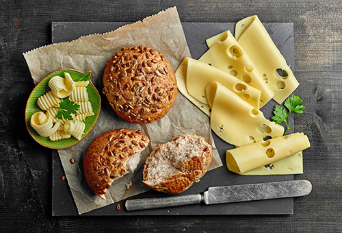 Körnerbrötchen auf Brettchen mit Käsescheiben daneben