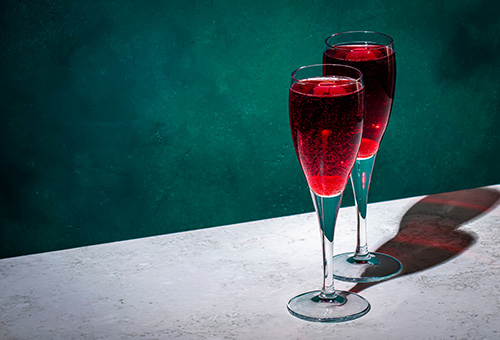 Kir Breton Zwei Gläser mit Kir Breton, Aperitif auf Johannisbeerlikör und Cidre, auf einem Tisch vor einer grünen Wand
