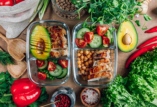 Meal Prep Hühnchen mit Gurken-Tomatensalat und Avocado in zwei Glasschüsseln