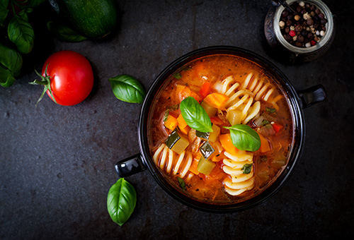 Minestrone in einer schwarzen Suppenschüssel auf einem dunkeln Tisch von oben fotografiert