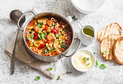 Minestrone im Topf auf einem Tisch mit gröstetem Brot und Parmesan