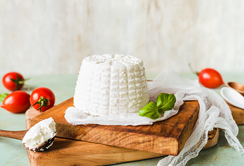 Ricotta auf einem Holzbrett, Tomaten im Hintergrund als Dekoration