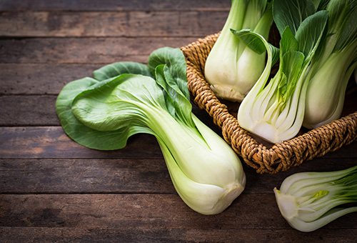 Pak Choi Zwei ganze und ein halber Pak Choi in einem Korb und ein ganzer und ein halber Pak Choi auf dem Tisch davor