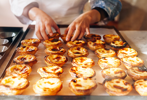 Pastéis de Nata frisch aus dem Backofen mit Bäckerin im Hintergrund