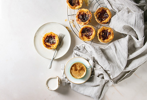 Pastéis de Nata auf einem Teller und auf einem Backblech